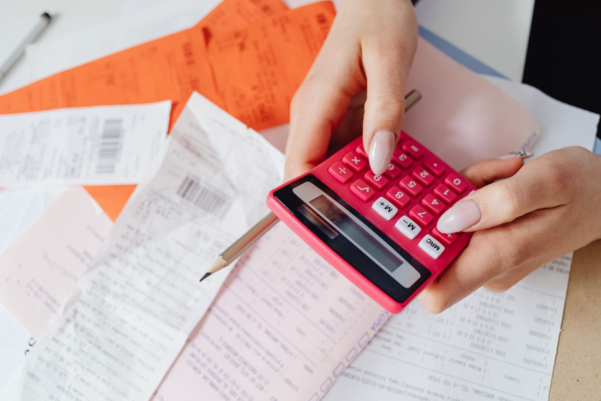 Mains utilisant une calculatrice rose pour gérer les dépenses